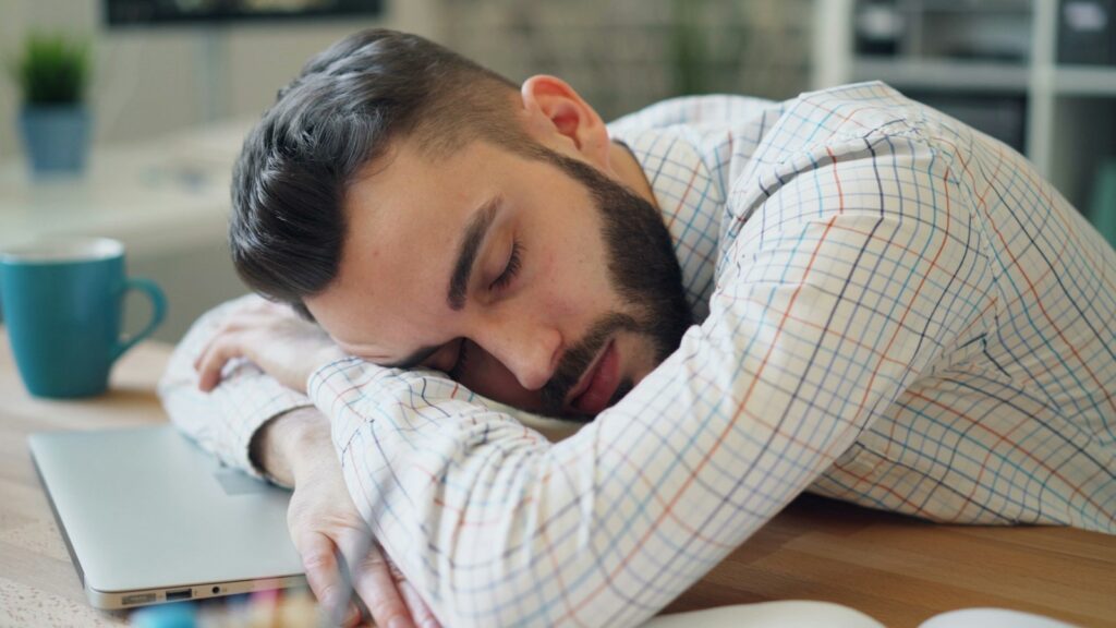 Homem cochilando com a cabeça apoiada sobre o notebook no trabalho