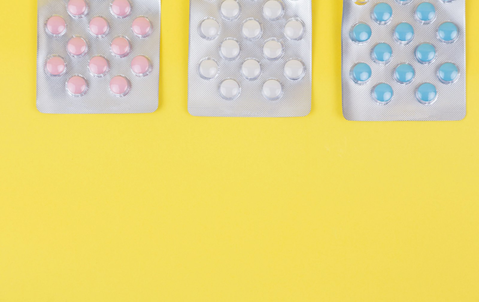 Comprimidos coloridos (rosa, branco e amarelo) organizados sobre fundo amarelo, representando pílulas usadas em estudos sobre suplementos e efeito placebo