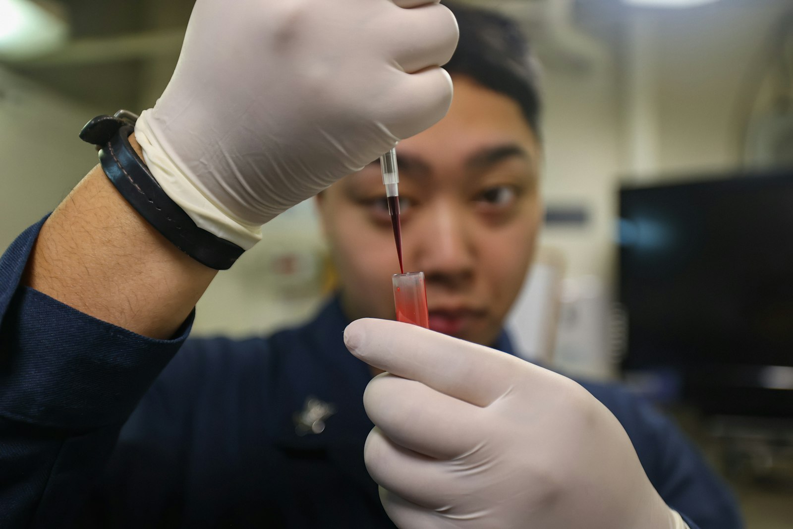 A person in gloves carefully transfers liquid into a vial